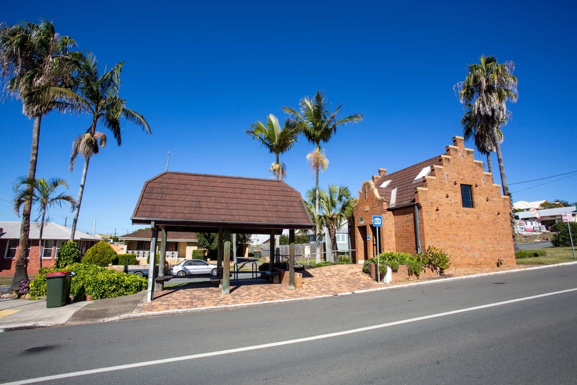 A Brick Building With Palm Trees In Front Of It — Tom Thumbs Tree Works In Kilcoy, QLD