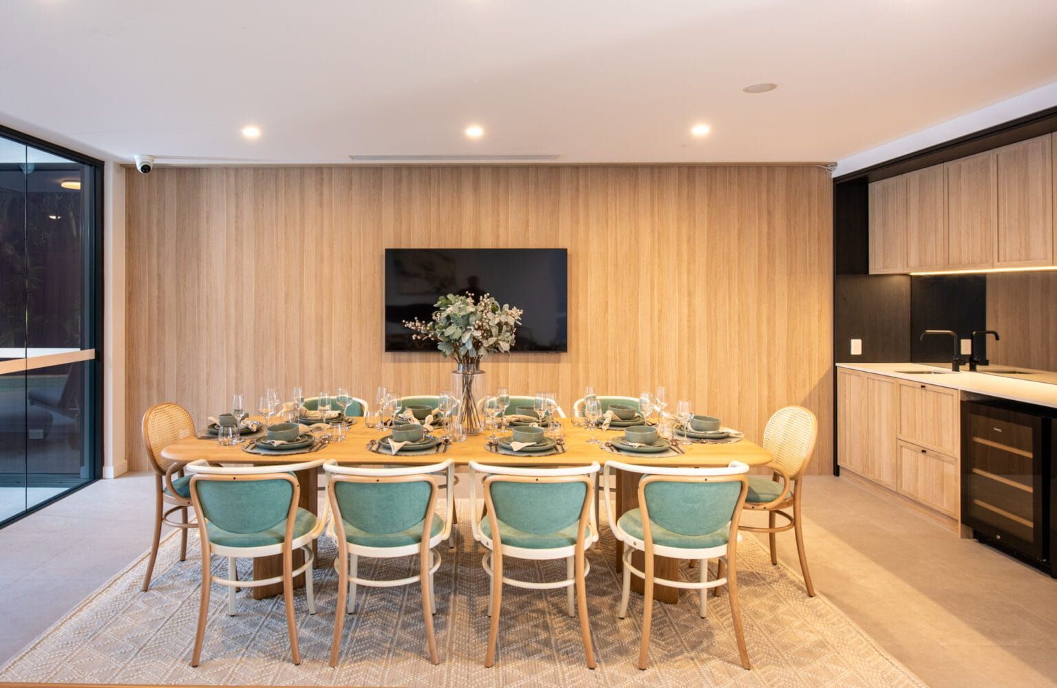 A Dining Room With A Long Table And Chairs And A Flat Screen Tv — Harrison Development Group In Surfers Paradise, QLD