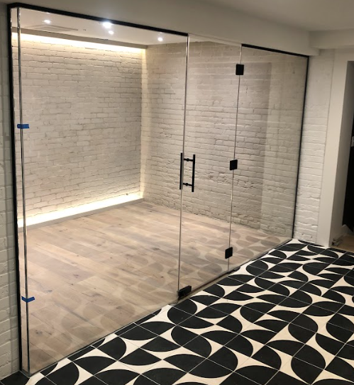 Glass-enclosed room with black trim, brick wall, and patterned floor, two glass doors with black handles.