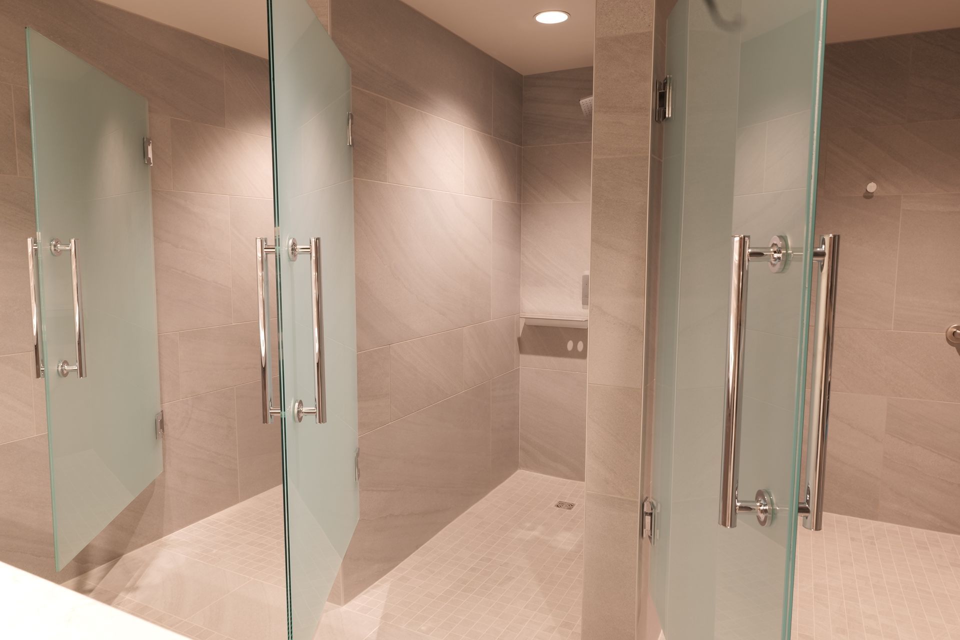 Three public showers with frosted glass doors, light gray walls, and silver hardware.