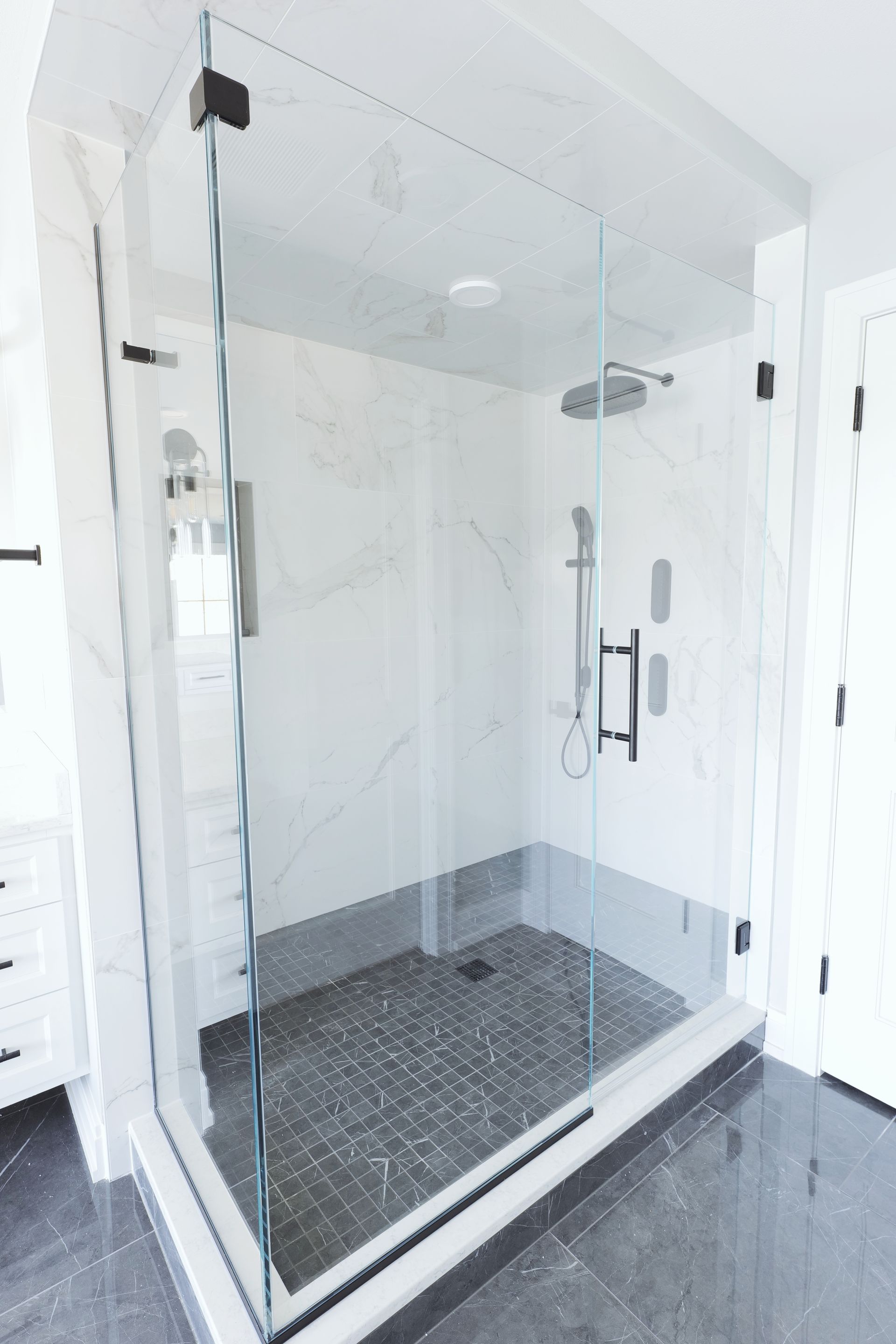 A modern, glass-enclosed shower with white marble walls and a dark gray tiled floor.