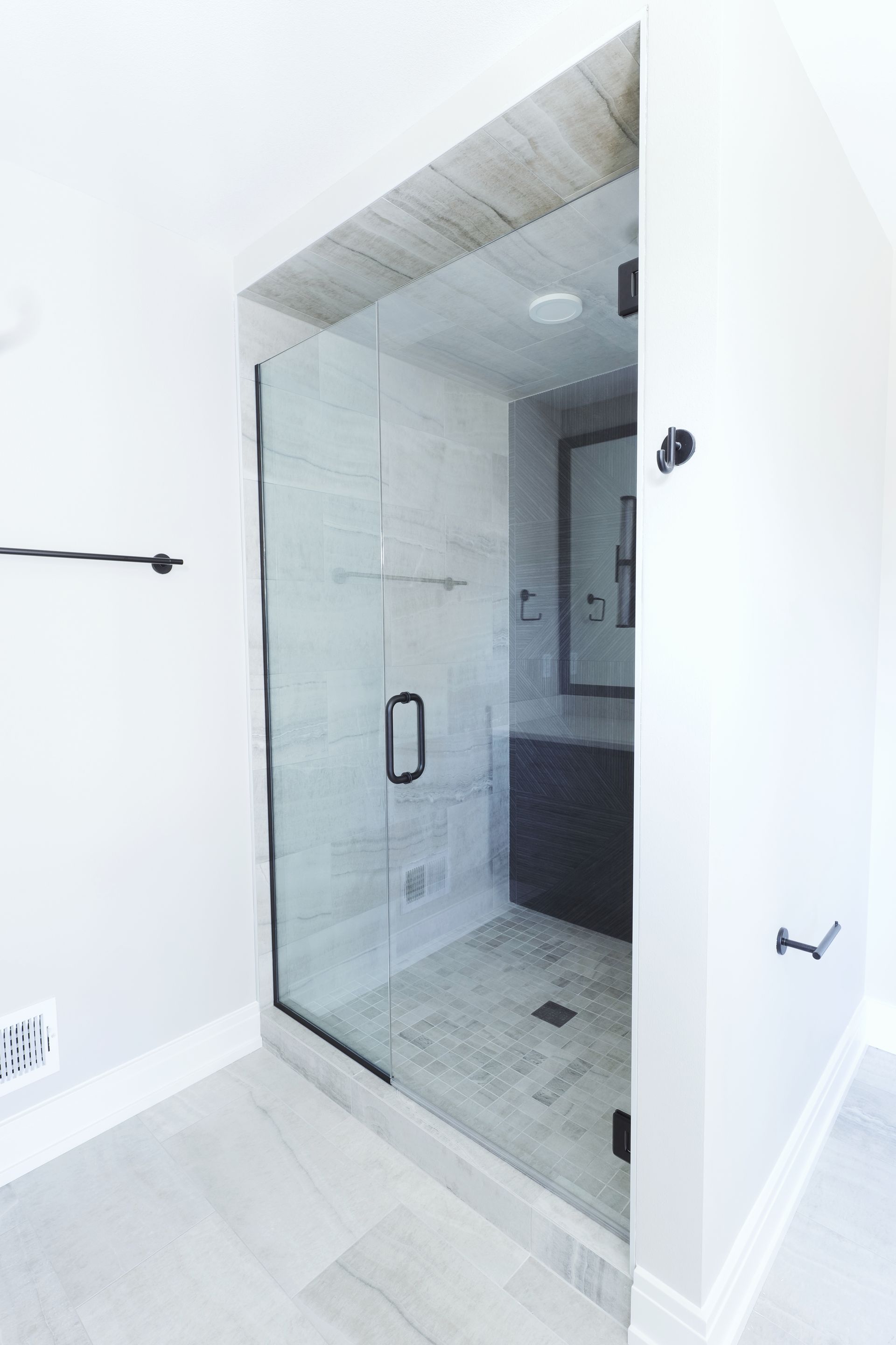 Modern bathroom with glass shower enclosure, gray tile floor, and black fixtures.