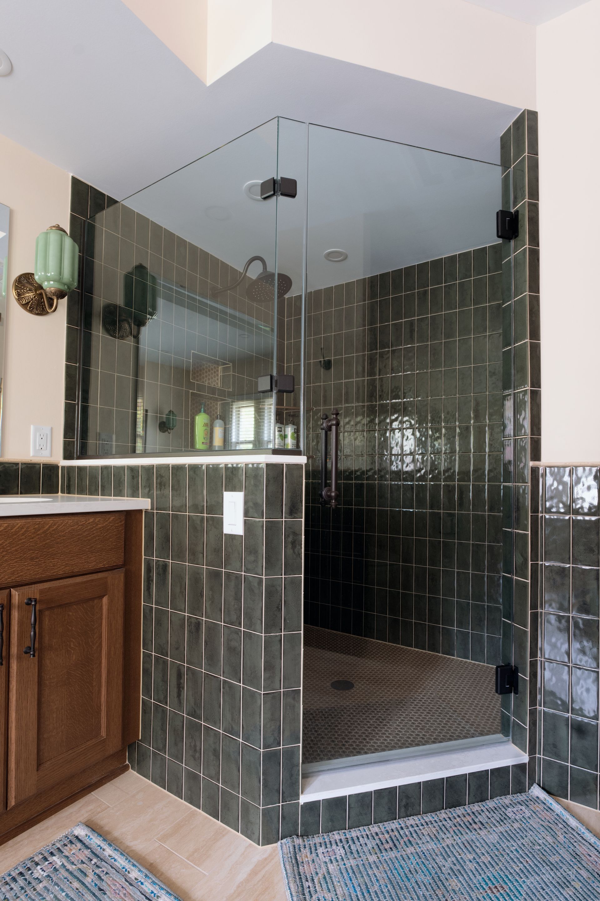Bathroom with dark tile shower and glass door. Brown vanity on the left.