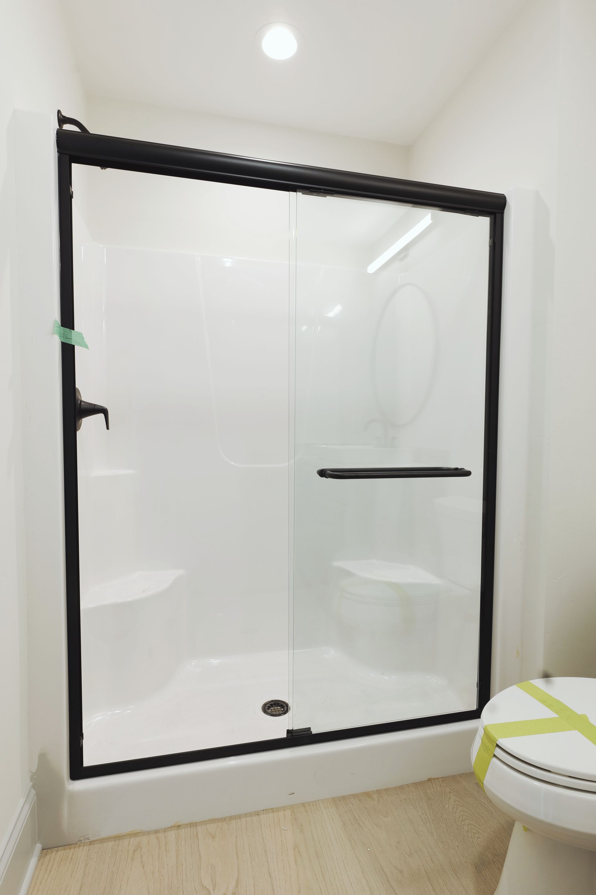 White shower stall with sliding glass doors, black frame, and a built-in seat.
