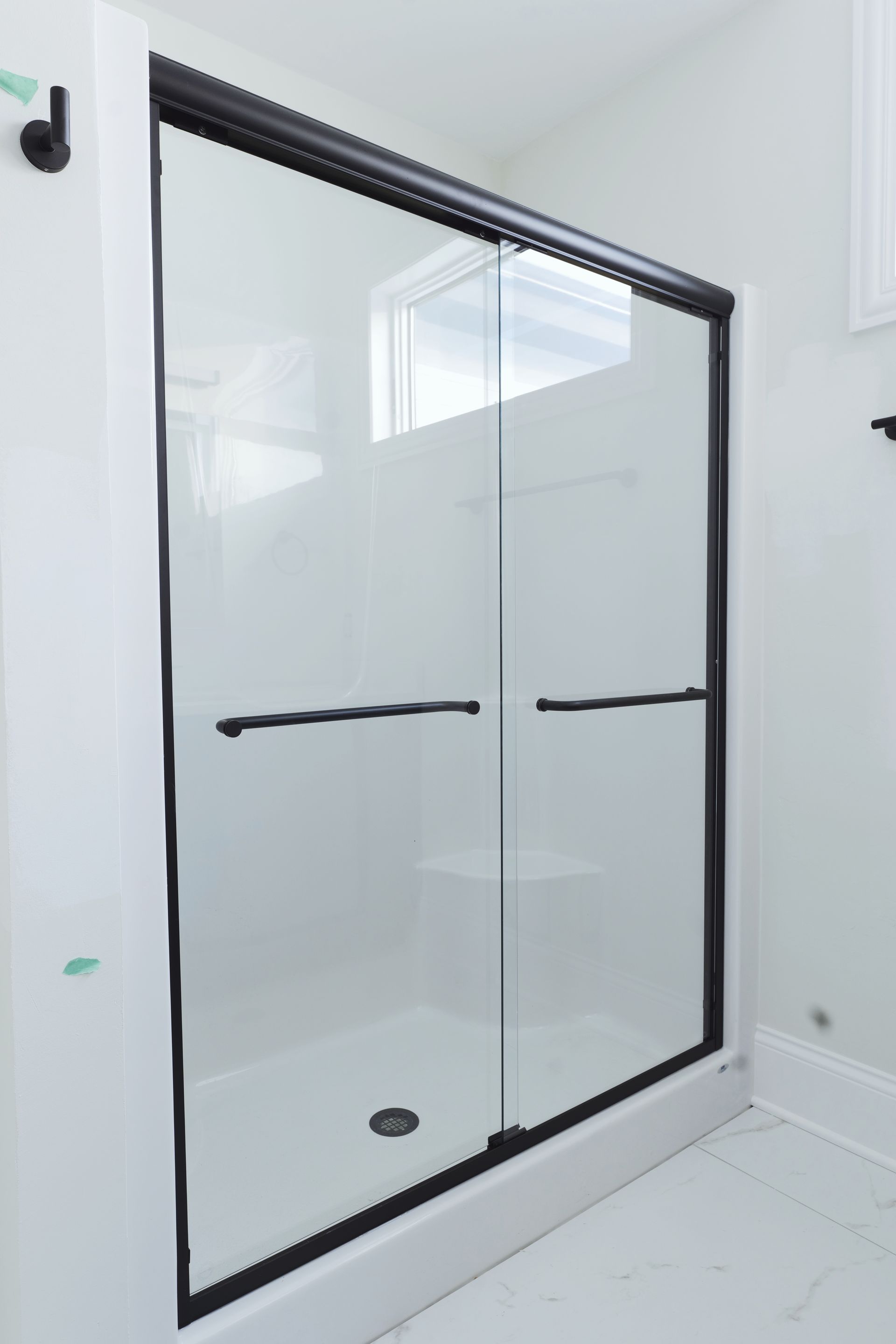 Black-framed glass shower enclosure in a white bathroom, with sliding doors and dark hardware.