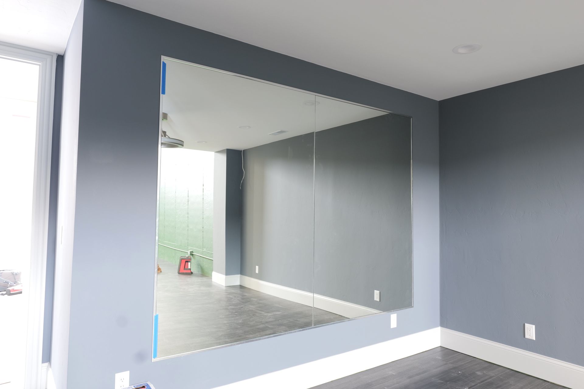 Large room with a mirrored wall and a person taking a photo; the floor is cement.
