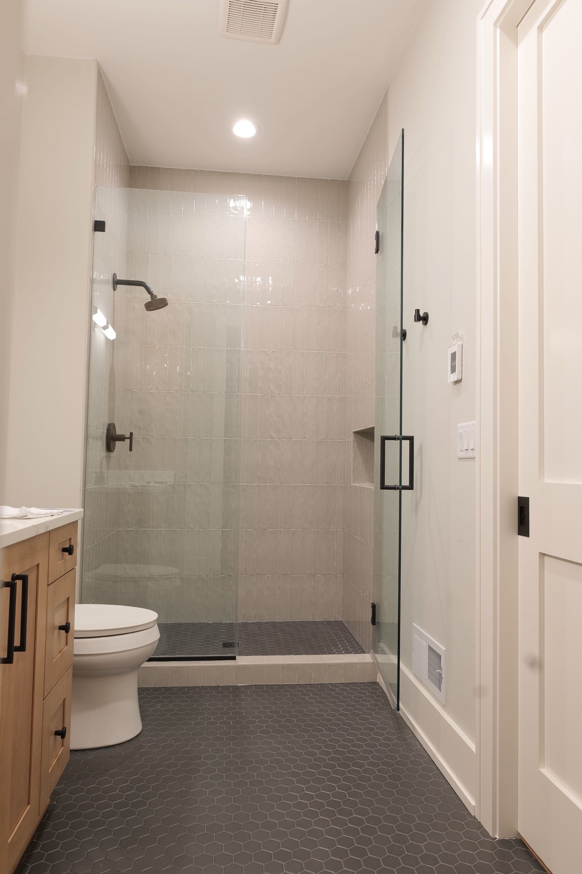 Bathroom with a glass shower, dark tile floor, and light wood vanity.