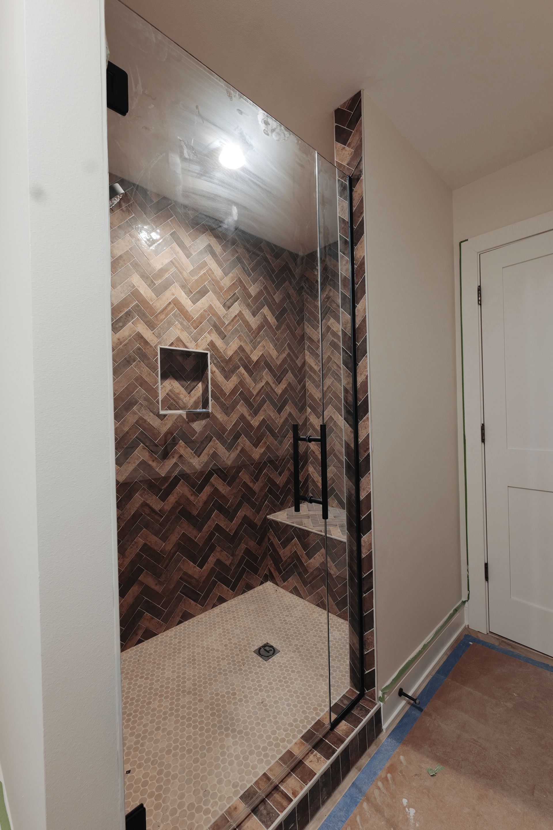 Glass-enclosed shower with brown chevron-patterned tile, small pebble floor, black hardware