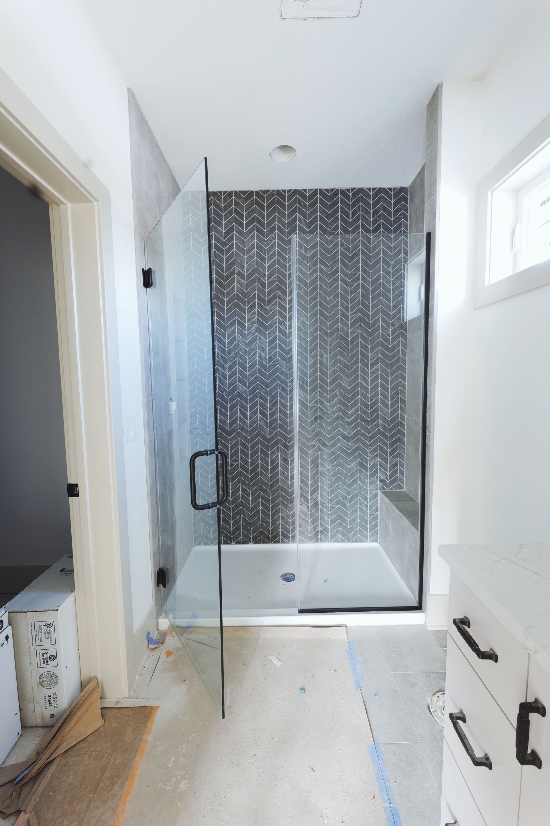 Modern bathroom with glass shower door, dark tile wall, white vanity.