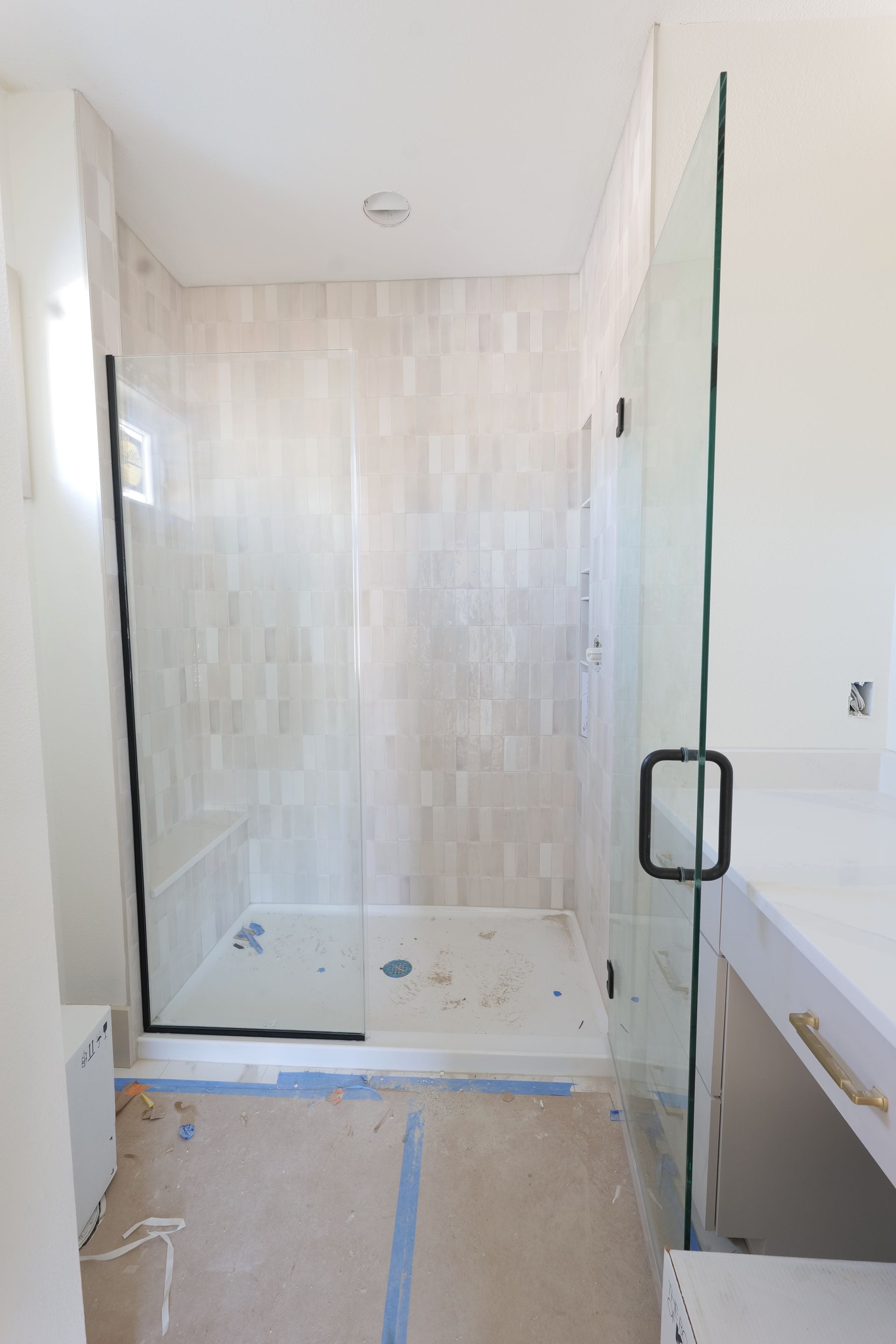 New shower with glass doors, white walls and tile, unfinished space.
