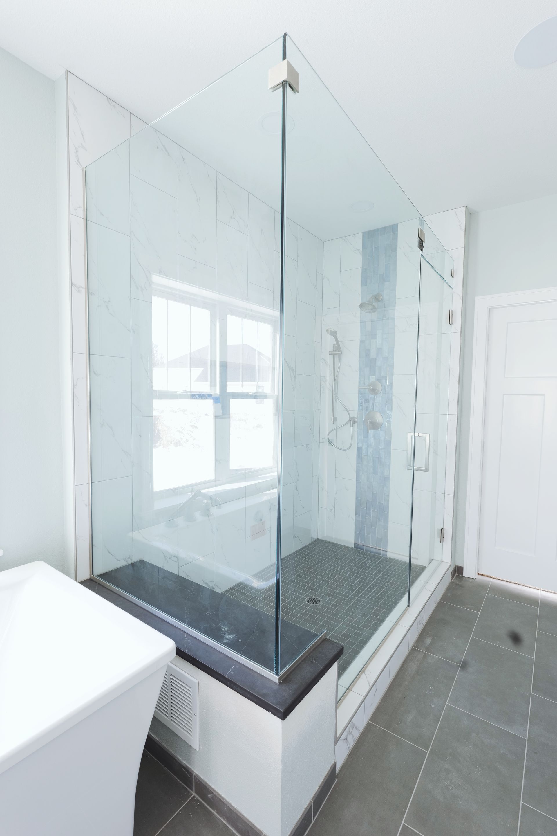 Corner shower with glass doors, black trim, and marble tile walls, beside a white vanity.