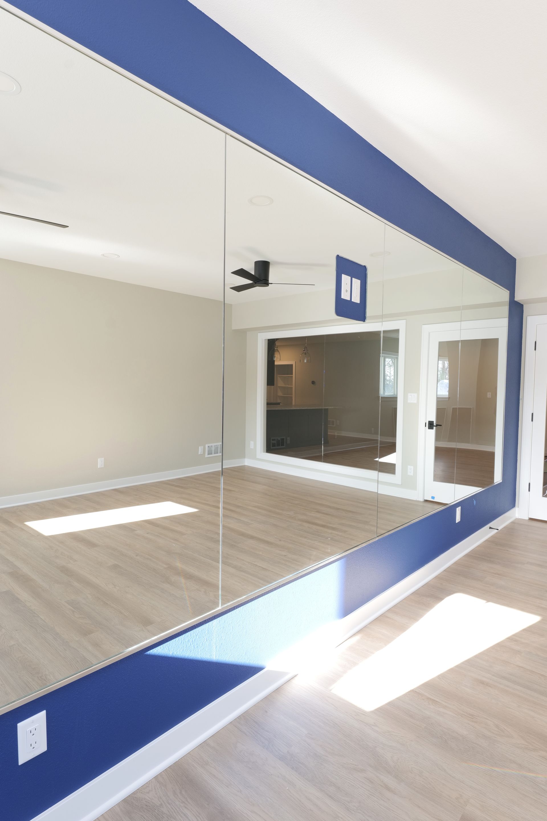 Room with large mirror on blue wall, reflecting interior space with sliding doors and light-colored floors.