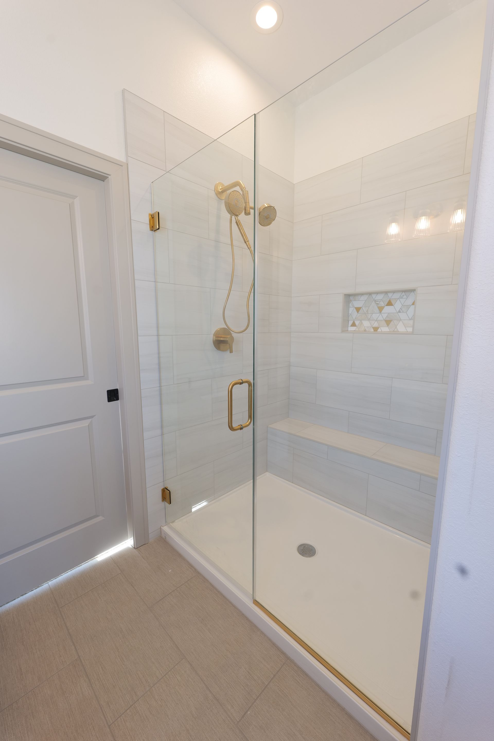 A bright white bathroom with a glass shower enclosure and gold fixtures.