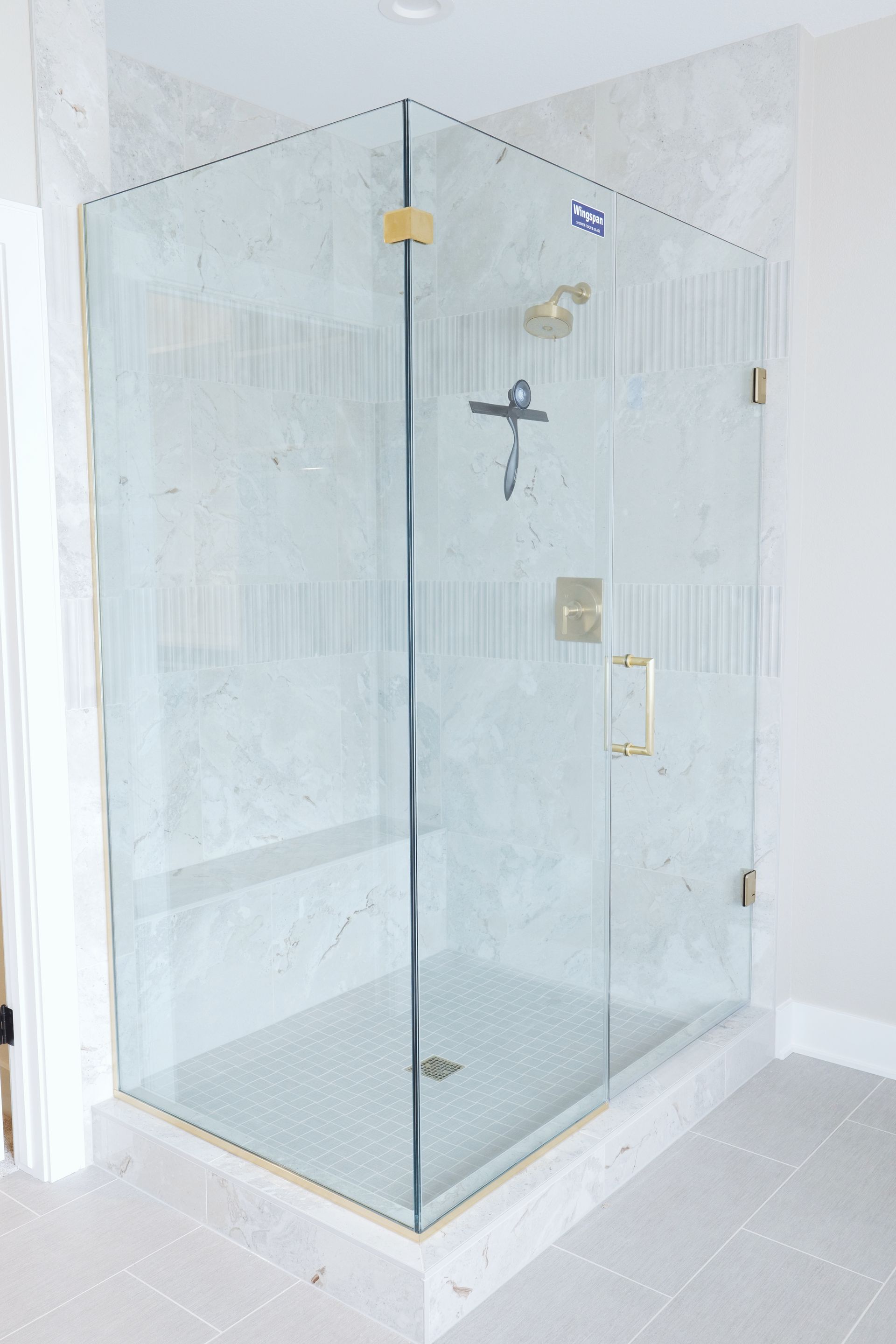 Glass corner shower with gold hardware, set on white tile.