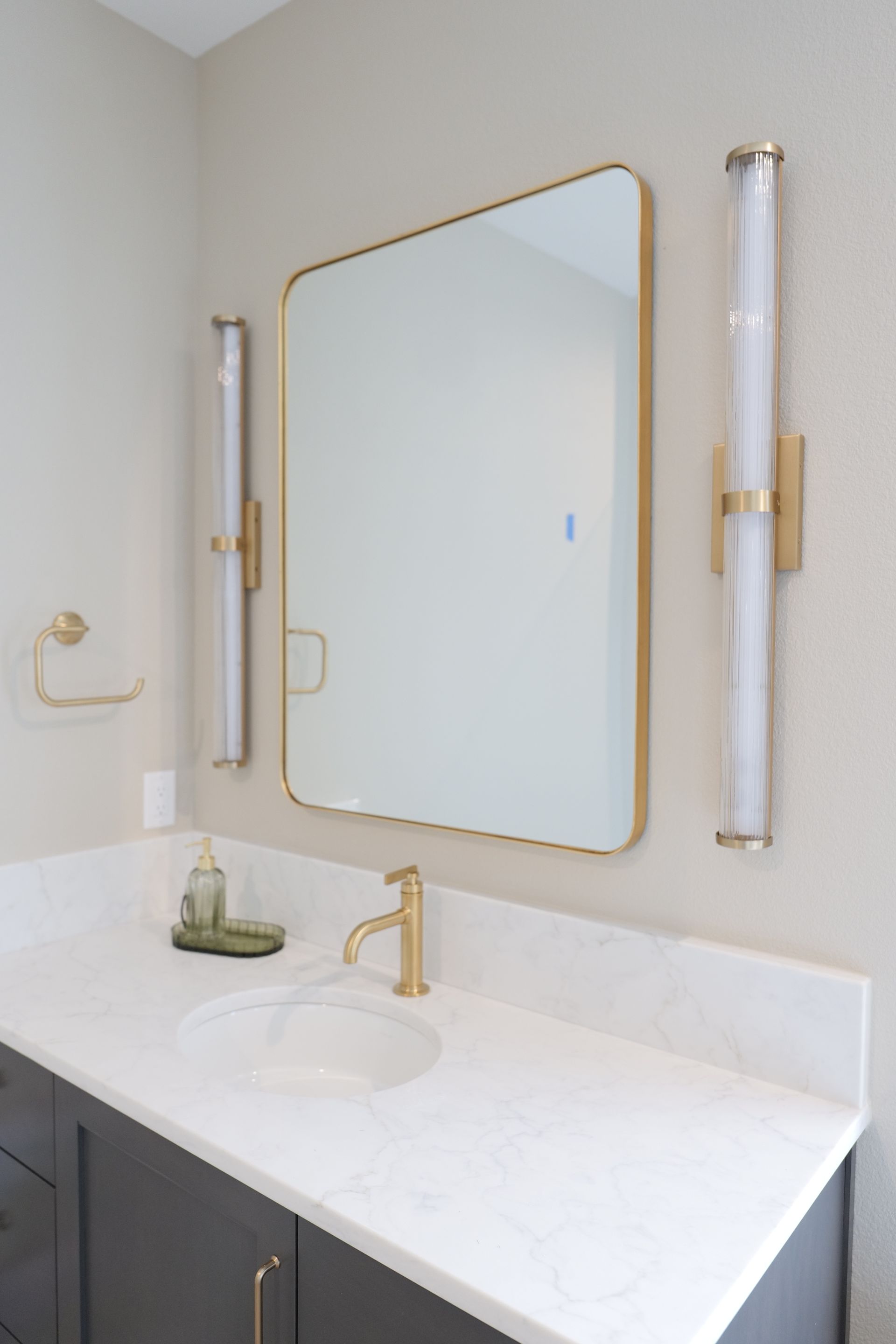 Bathroom with gold fixtures, a large mirror, and a white countertop.