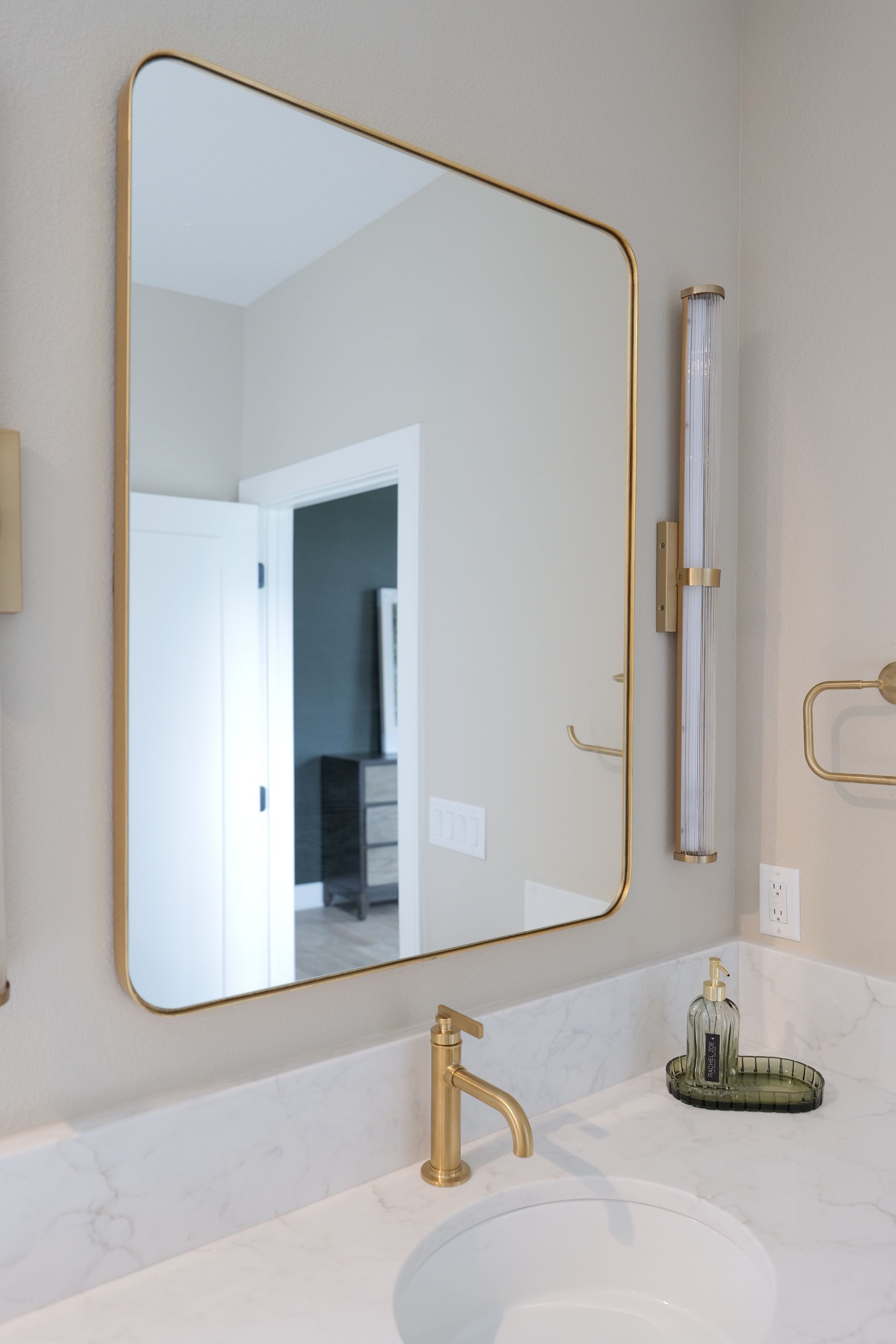 Bathroom with a gold-framed mirror over a white countertop with a gold faucet.