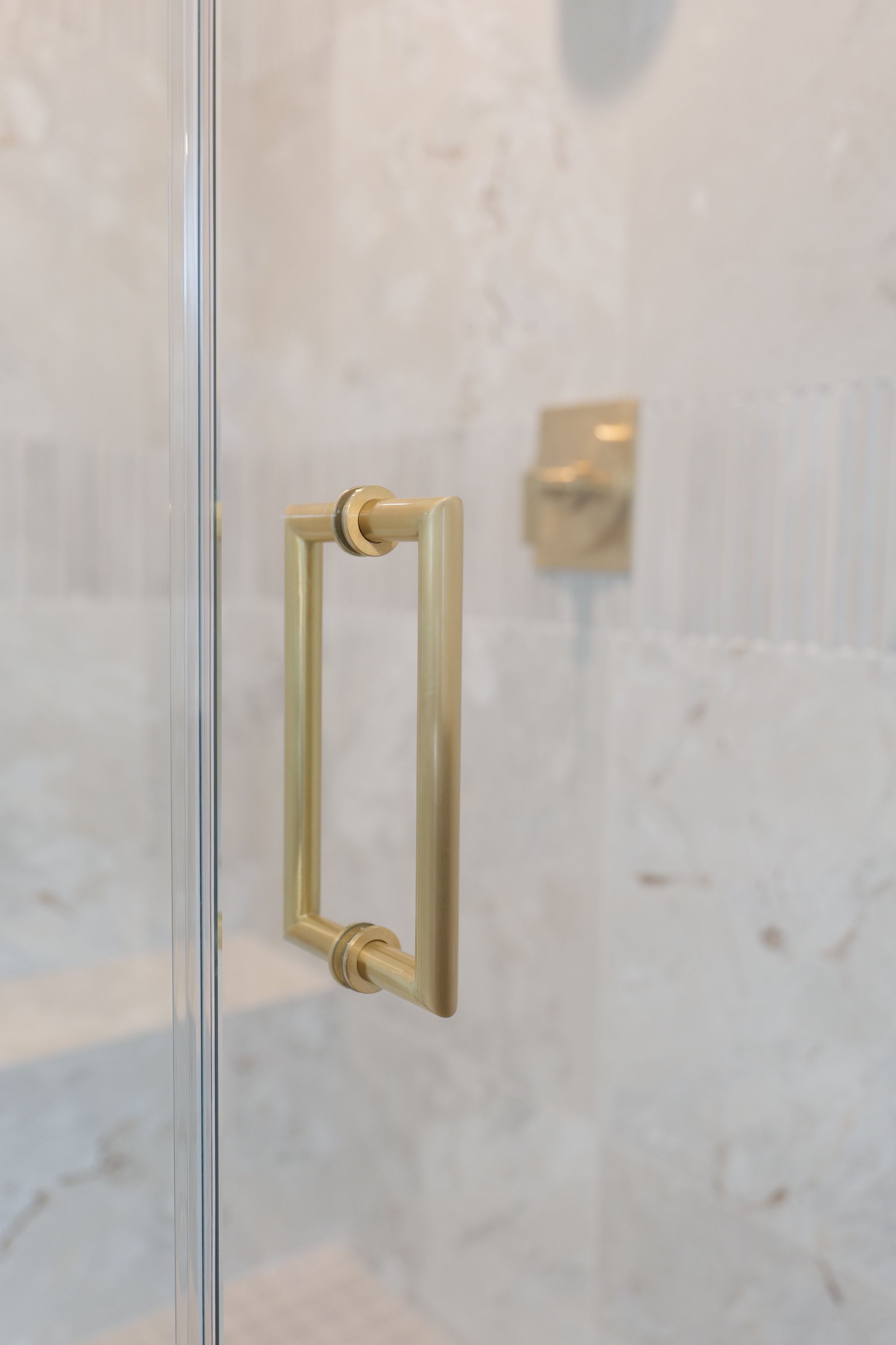 Gold shower door handle and square hardware against a marble wall.