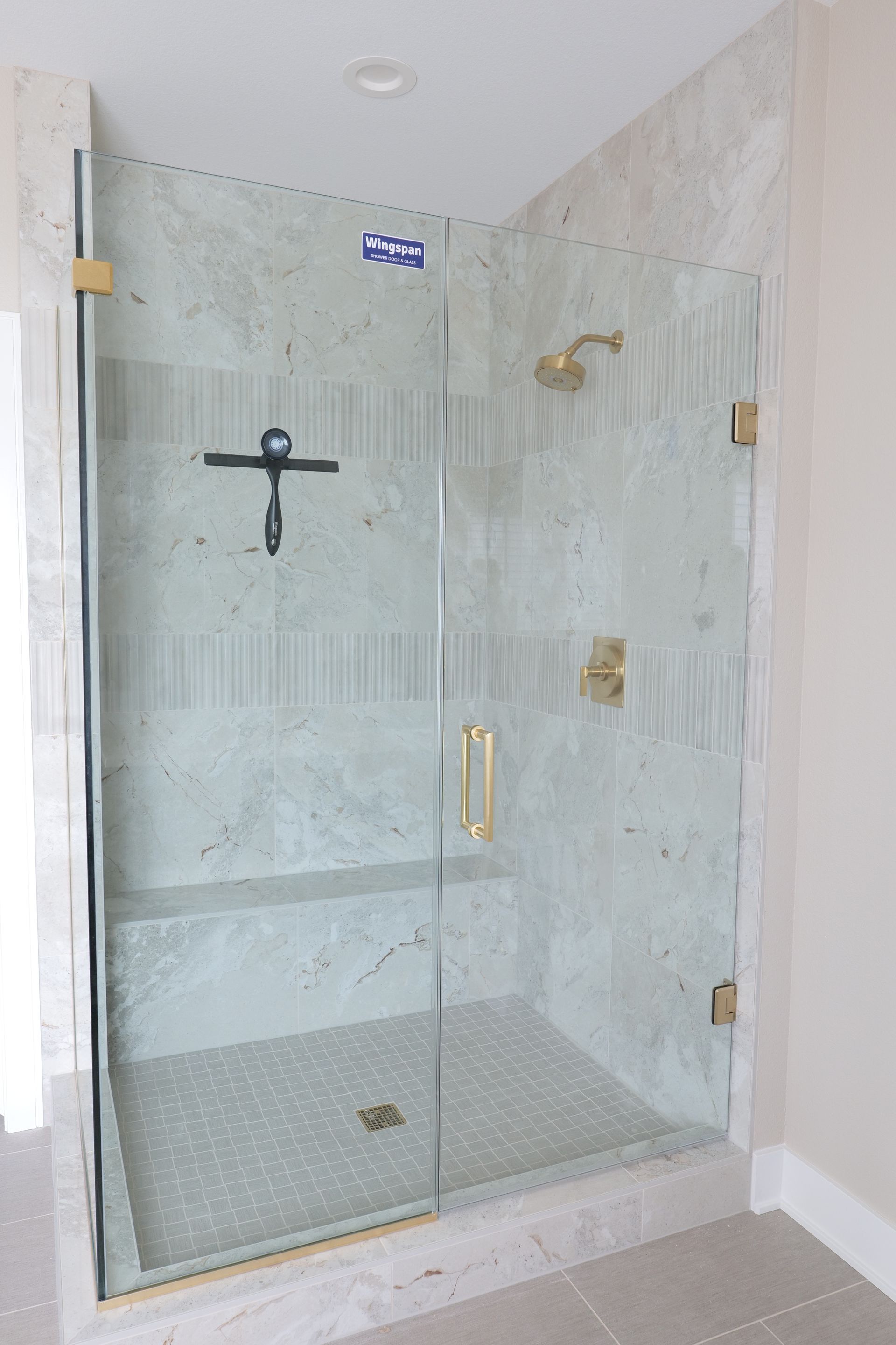 Shower stall with glass door, gold fixtures, and marble-look tile. Includes a built-in bench.