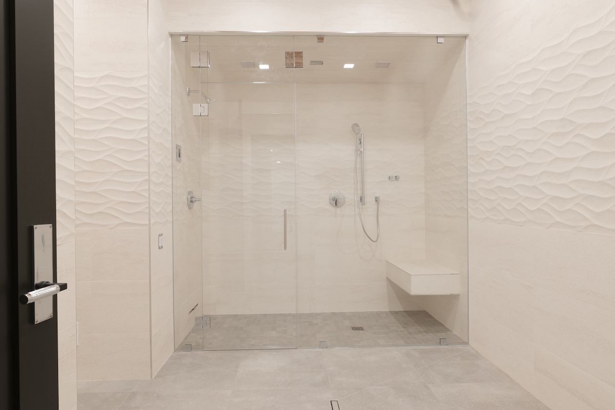 Modern, tiled bathroom with glass shower doors, white walls, and gray floor.