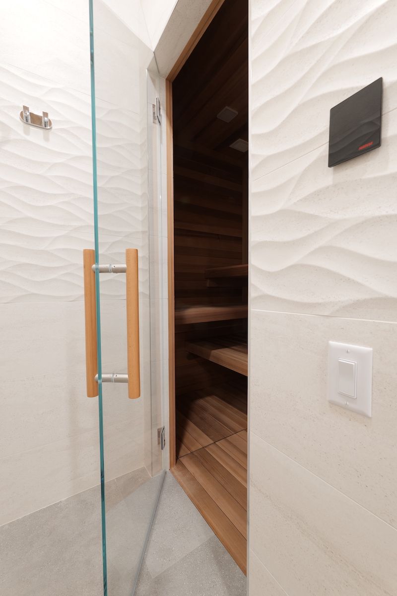 Glass door entrance to a sauna with wooden interior. White wavy-patterned wall.
