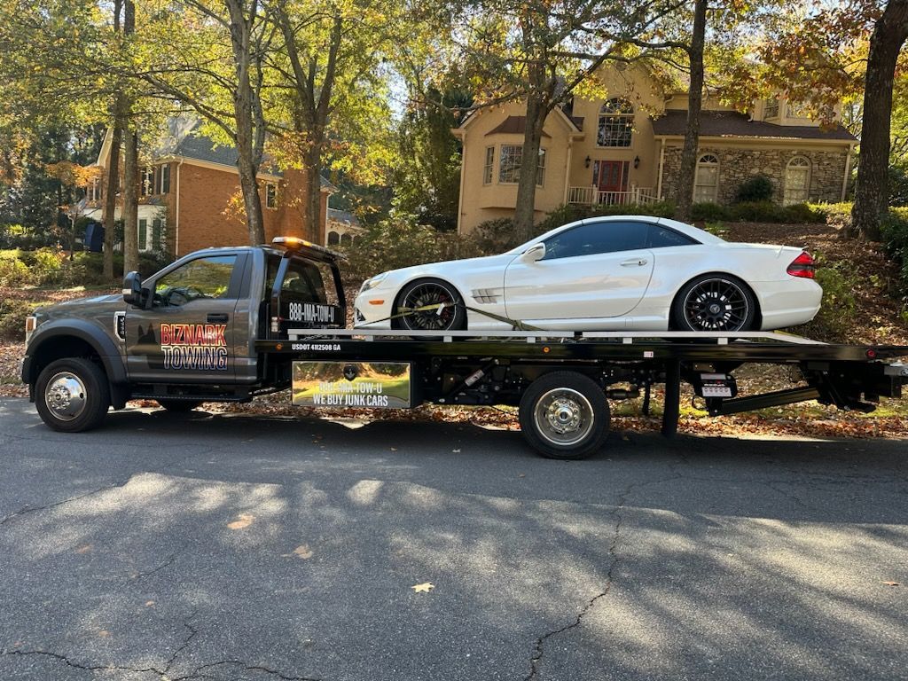 White sports car loaded on a flatbed tow truck on a residential street.