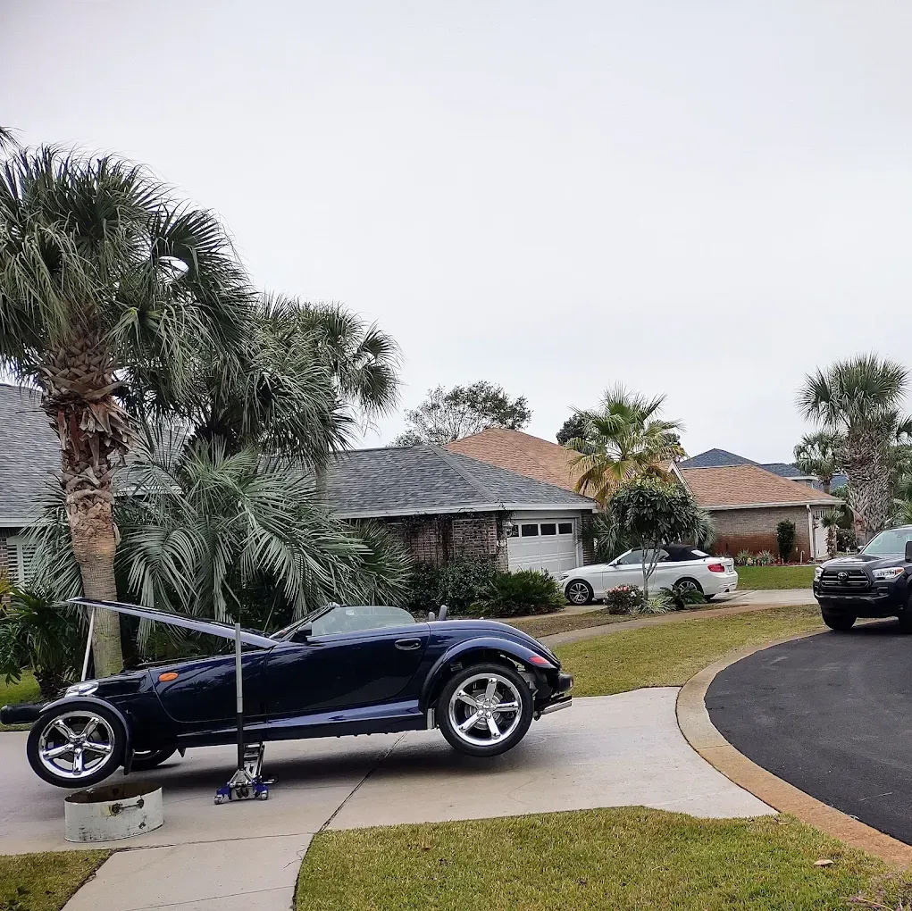 Dark blue Plymouth Prowler on jack in driveway, under overcast sky, neighborhood homes in background.