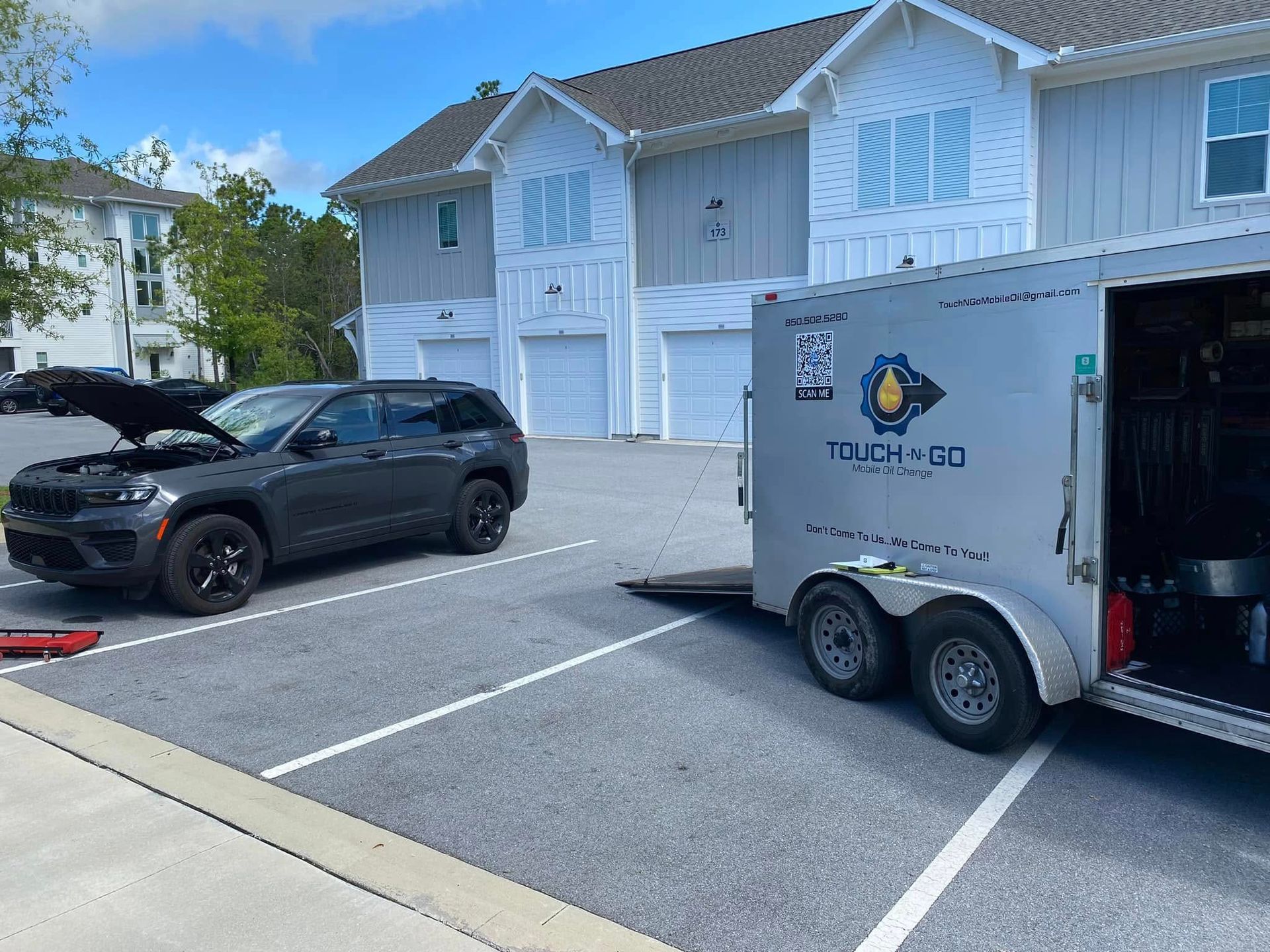 Gray SUV with open hood next to a trailer, in a parking lot in front of an apartment building.