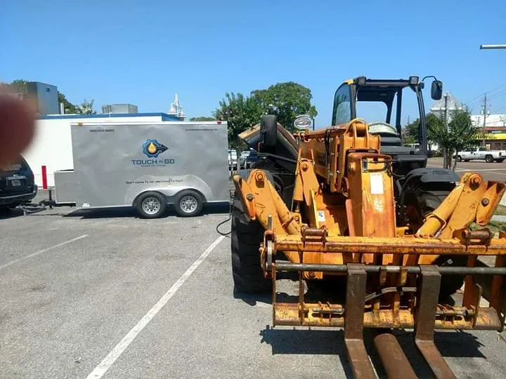 Forklift next to a trailer, both parked on a paved area on a sunny day.