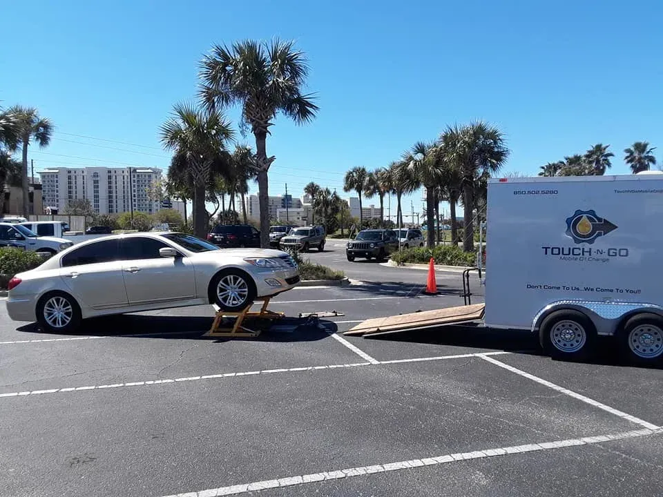 A silver car is lifted on a jack in a parking lot with a trailer labeled