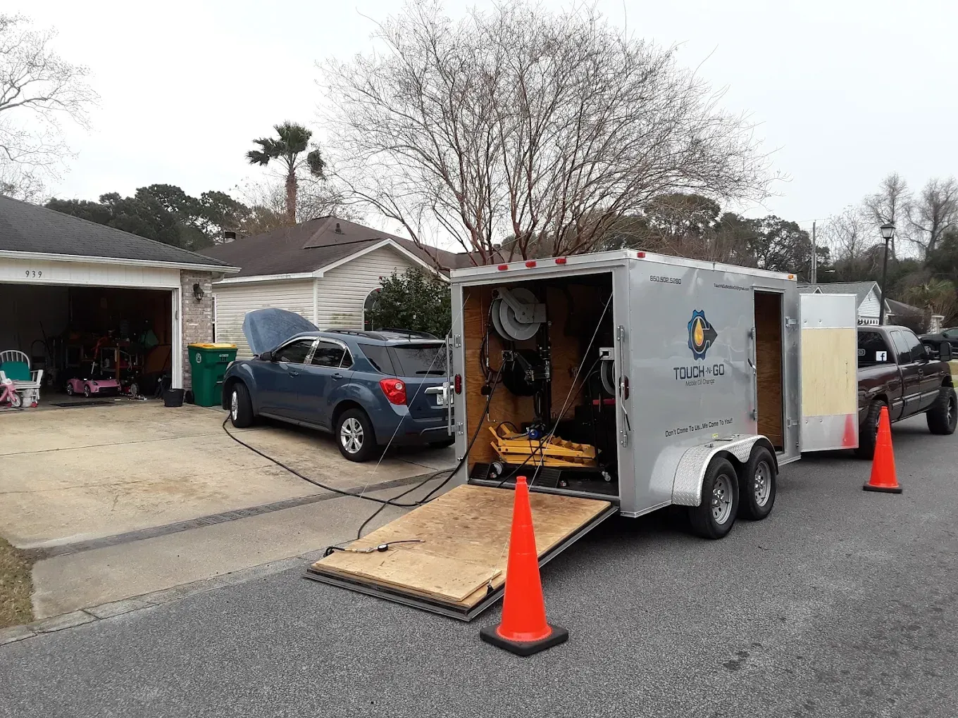 A blue car hooked up to a trailer with open doors and a ramp on a residential street.