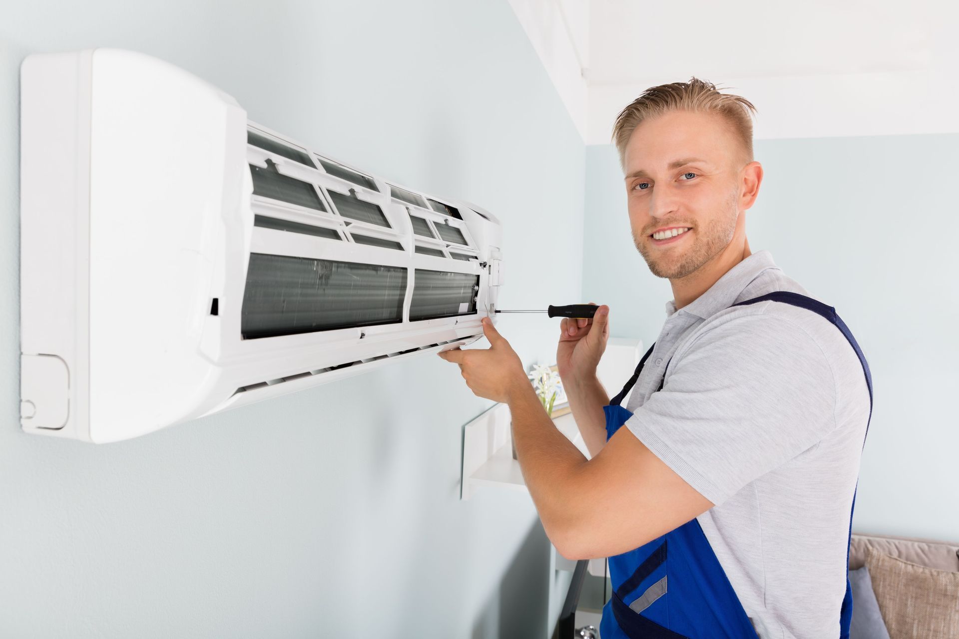 young male technician fixing air conditioner