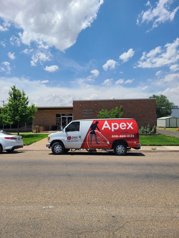 An apex van is parked on the side of the road in front of a building.