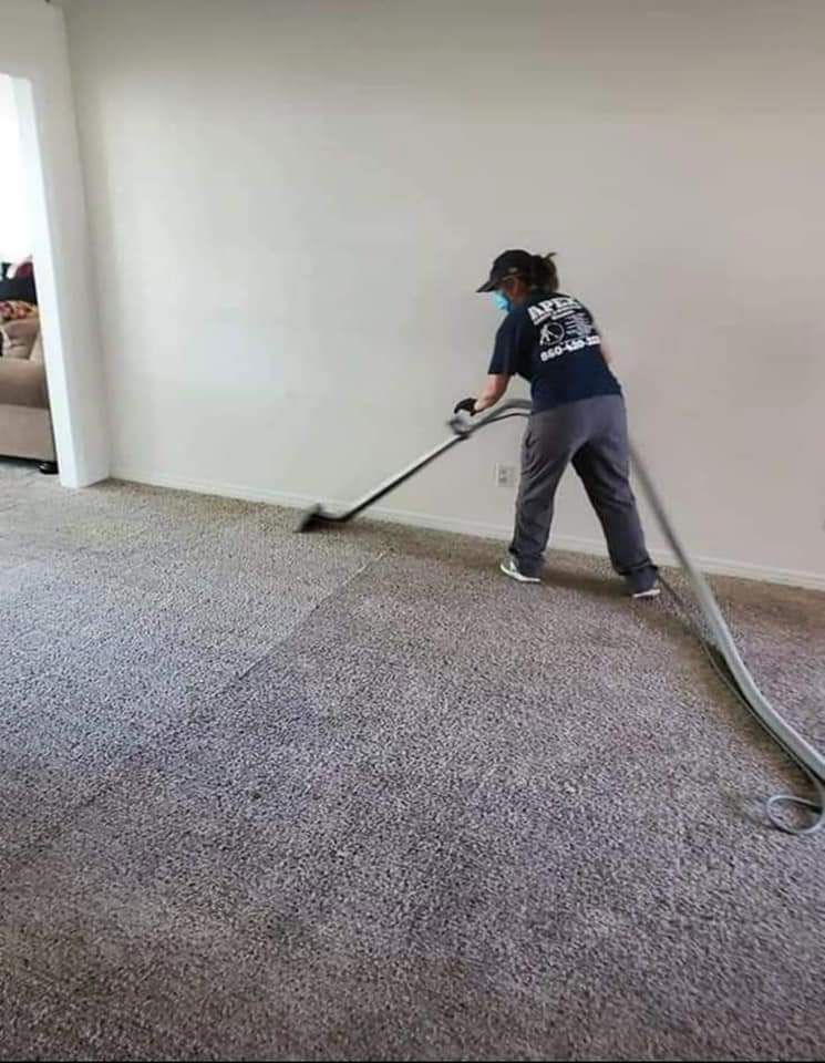 A woman is cleaning a carpet with a vacuum cleaner in a living room.