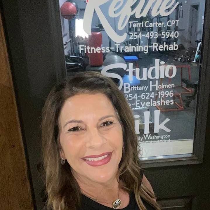 A woman is smiling in front of a gym door.