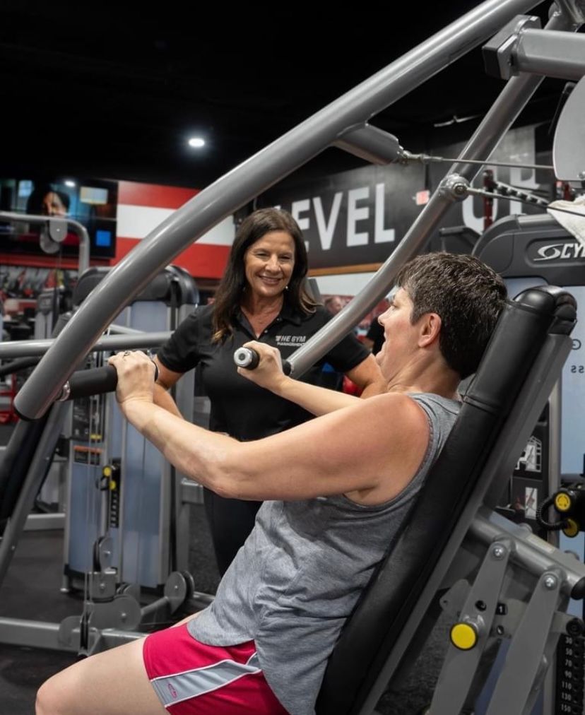 A woman is talking to a man on a machine in a gym.