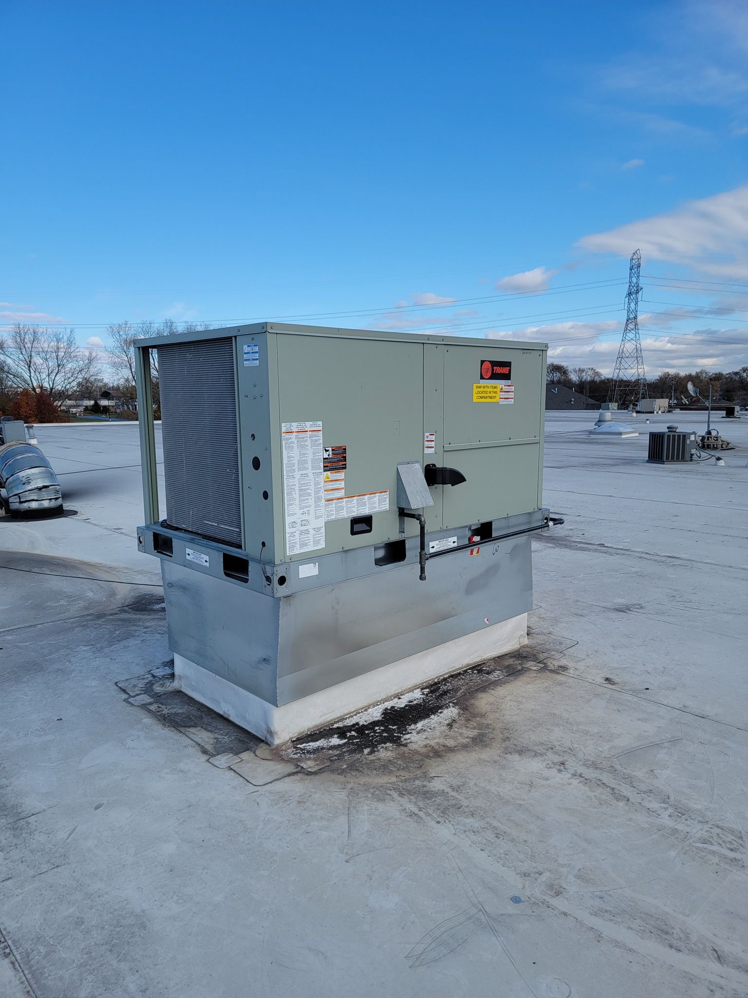 Rooftop HVAC unit on a white roof, under a blue sky. A tall communications tower visible in the background.