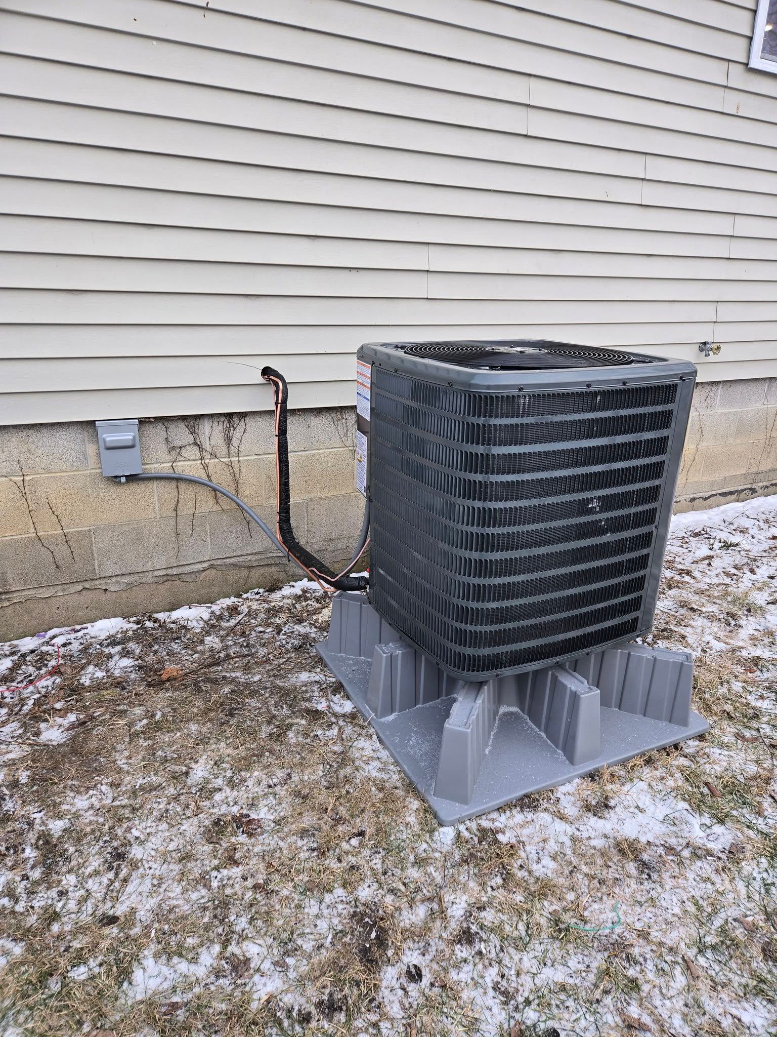 Outdoor air conditioning unit next to a house with winter snow on the ground.