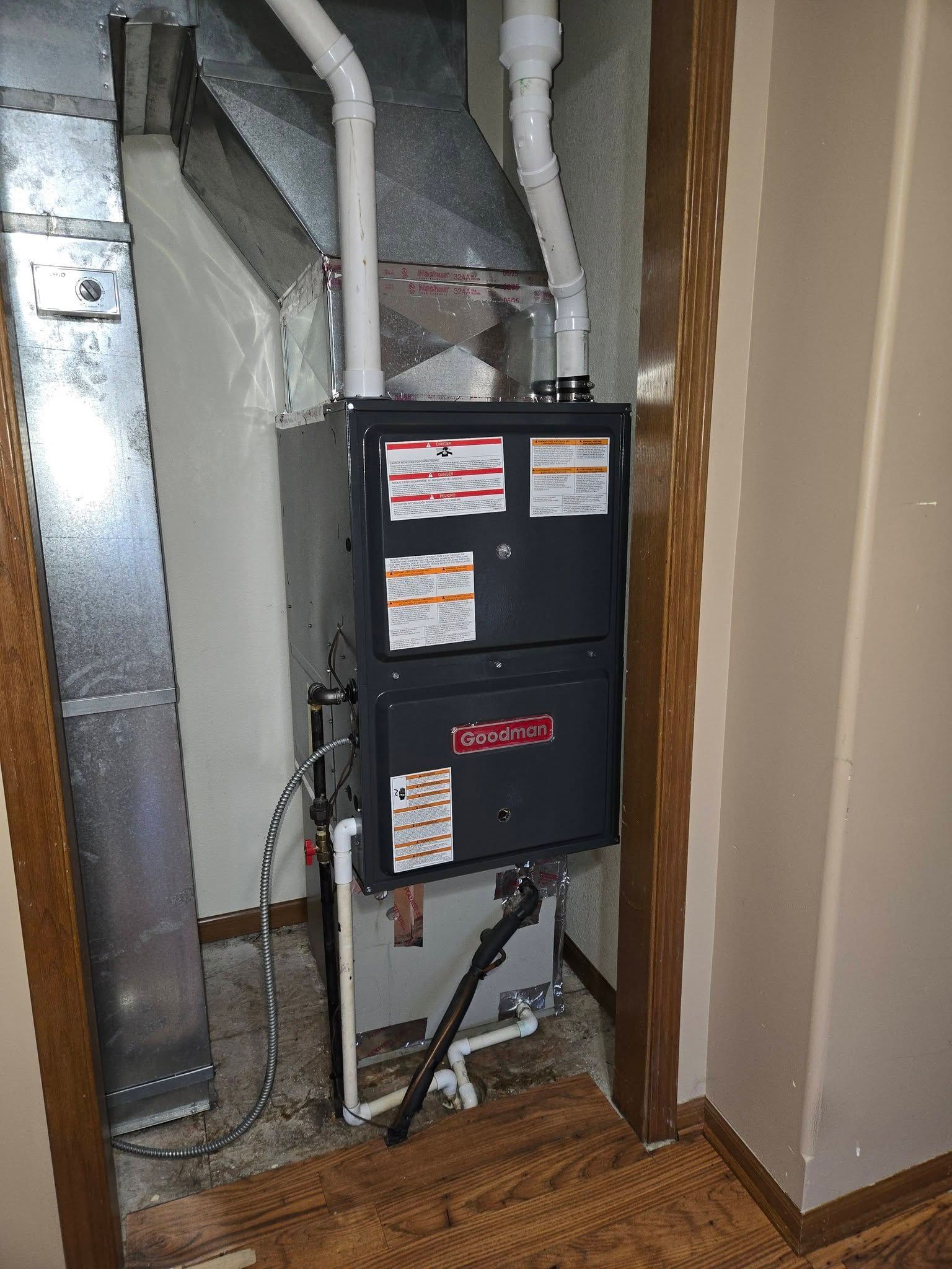 Furnace installed in a closet; silver, gray, and white with attached pipes and ductwork.