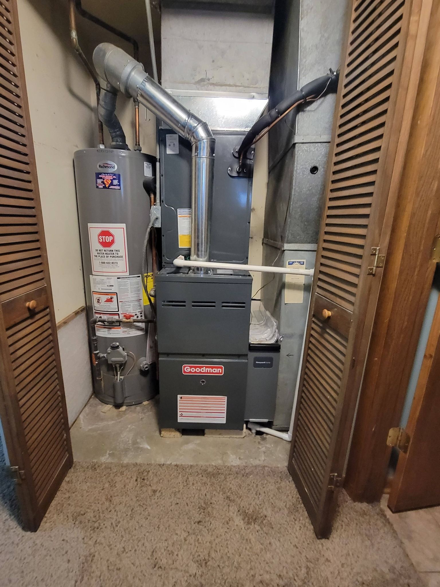 Furnace, water heater, and ductwork in a utility room, flanked by wood louvered doors.