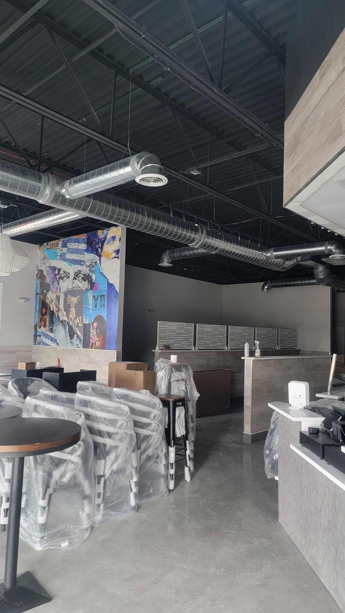 Interior of a new business with construction still in progress. Chairs wrapped in plastic, exposed ceiling with ventilation.
