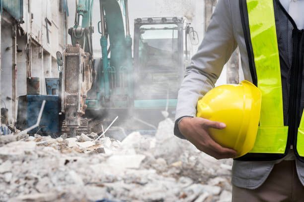 A construction worker in a hard hat and vest stands in front of a building, ready for demolition.