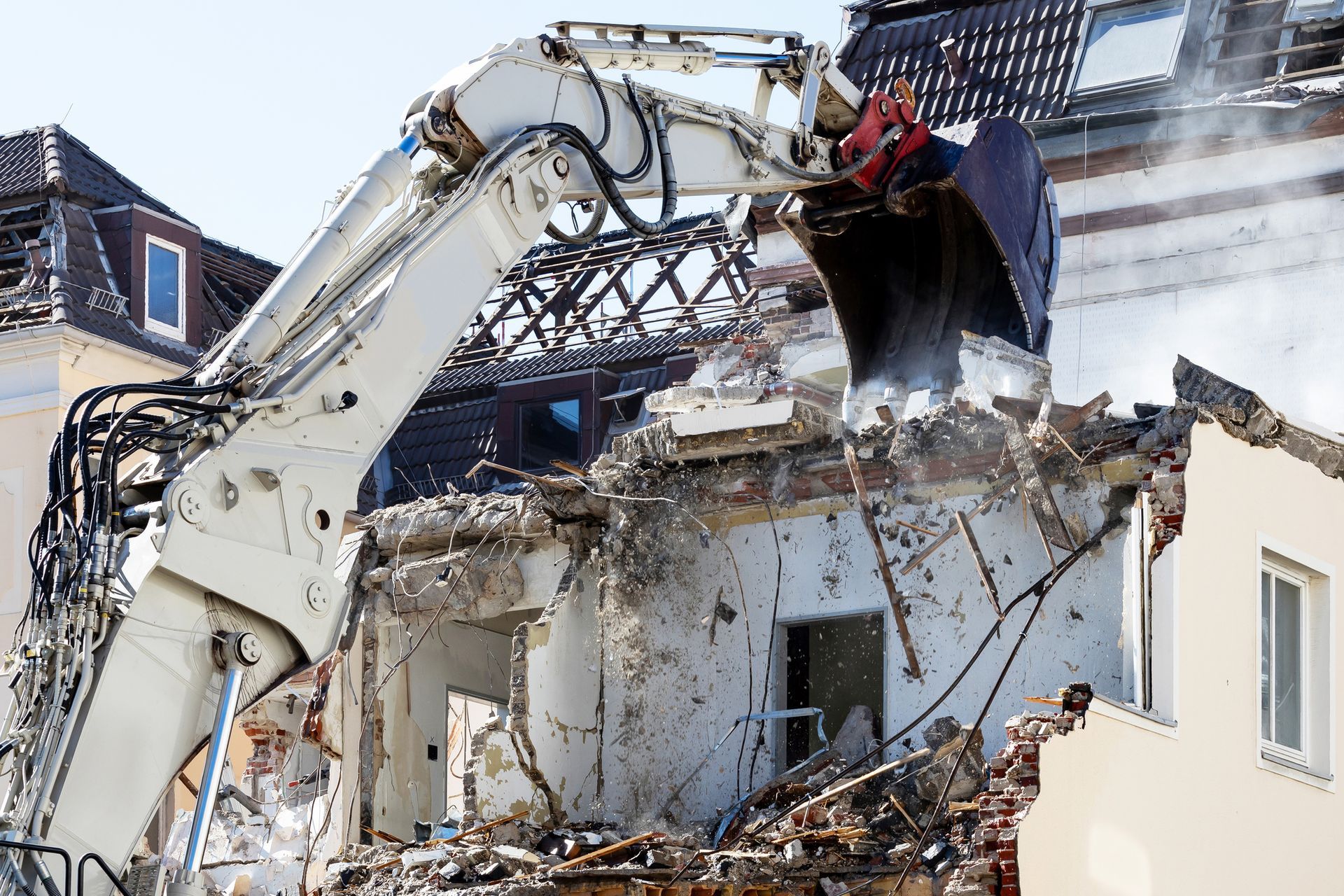 Excavator performing building demolition, tearing down house structure during daytime operation.