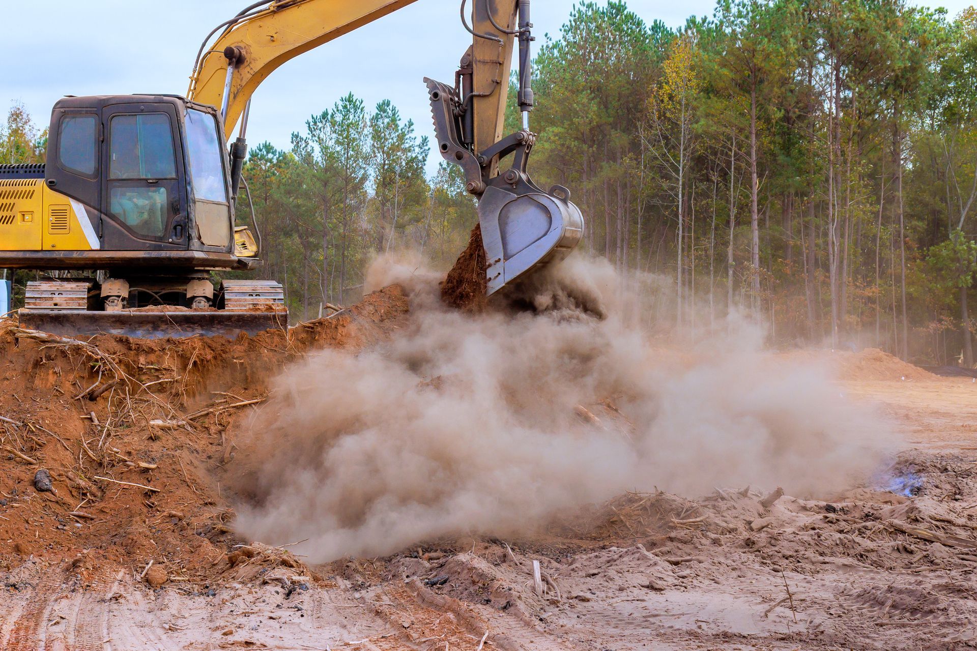 Excavator clearing soil at construction site with dust rising during land preparation work today task.