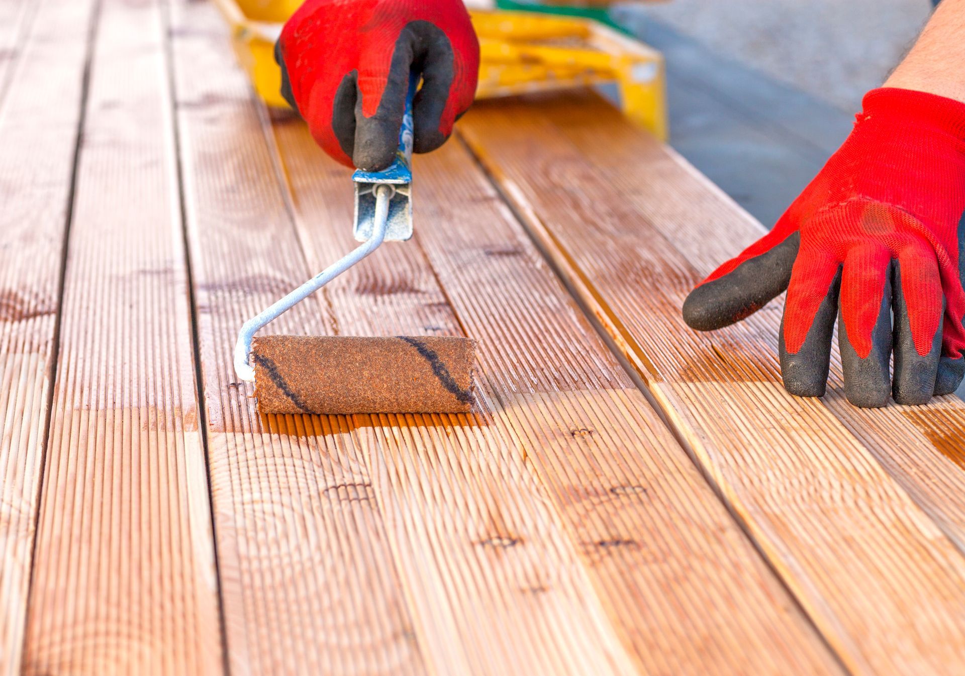 A person is painting a wooden deck with a roller.