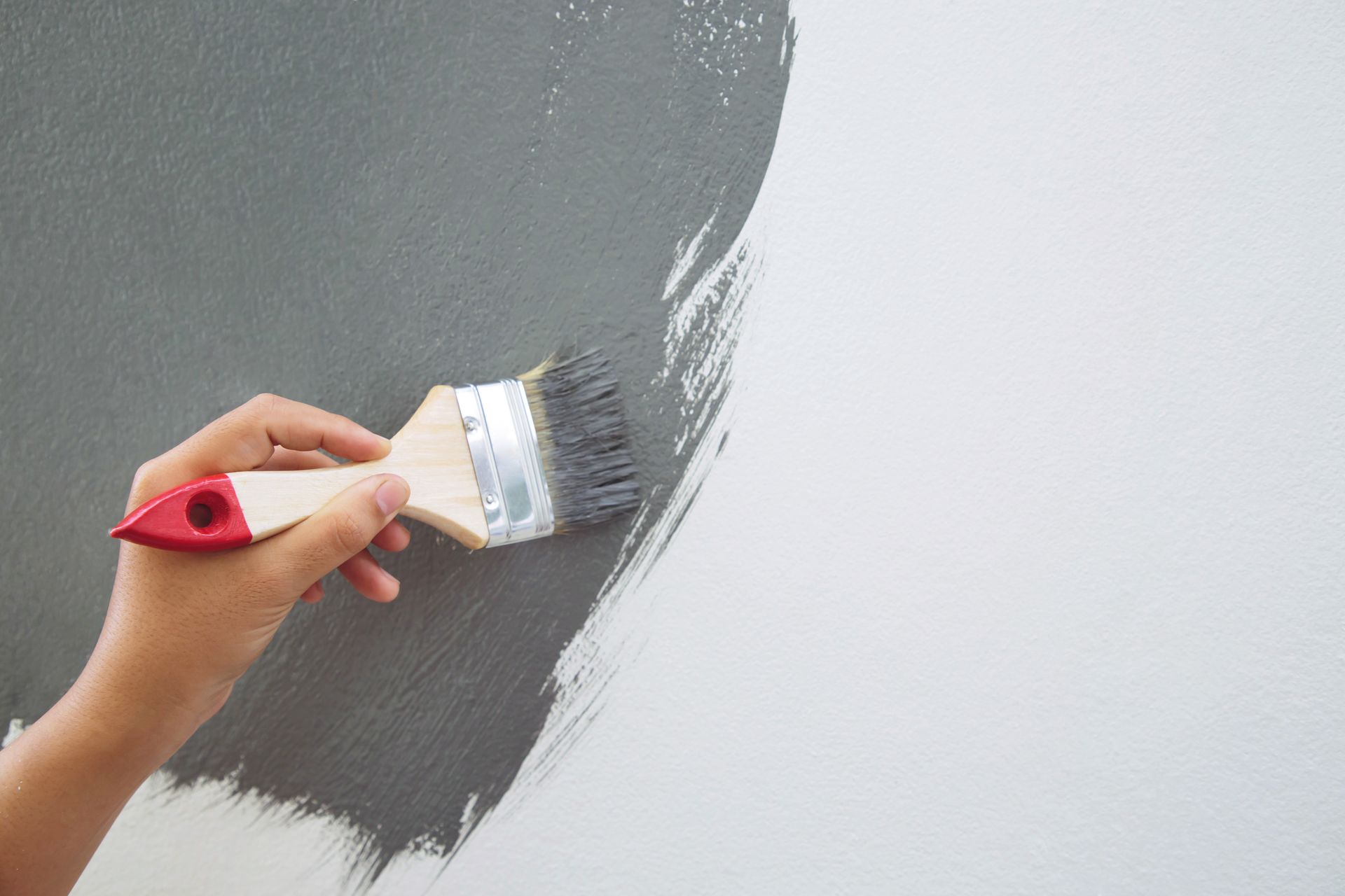 A person is painting a wall with a paint brush.