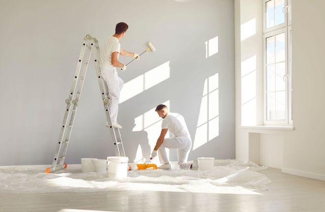 Two men are painting a wall in an empty room.