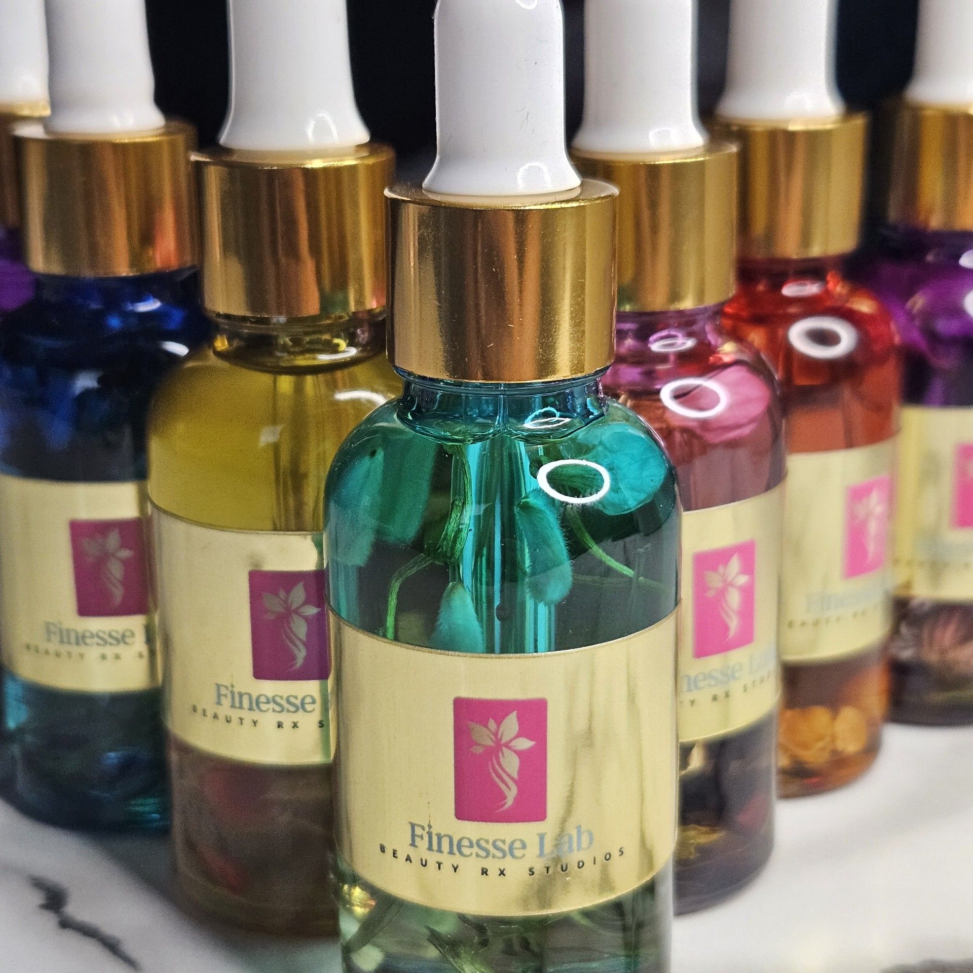 Close-up of several small glass bottles filled with colorful liquid. Each has a gold cap and a label.