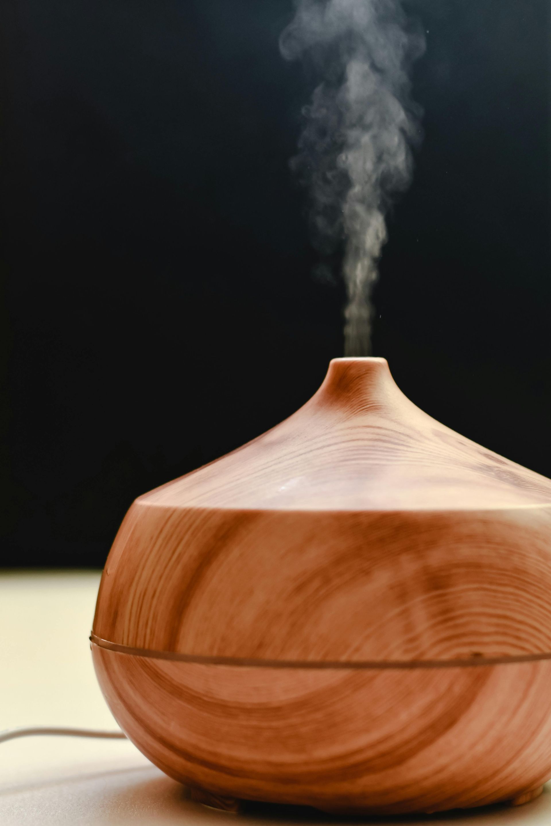 Wooden essential oil diffuser emitting a plume of vapor, against a black background.