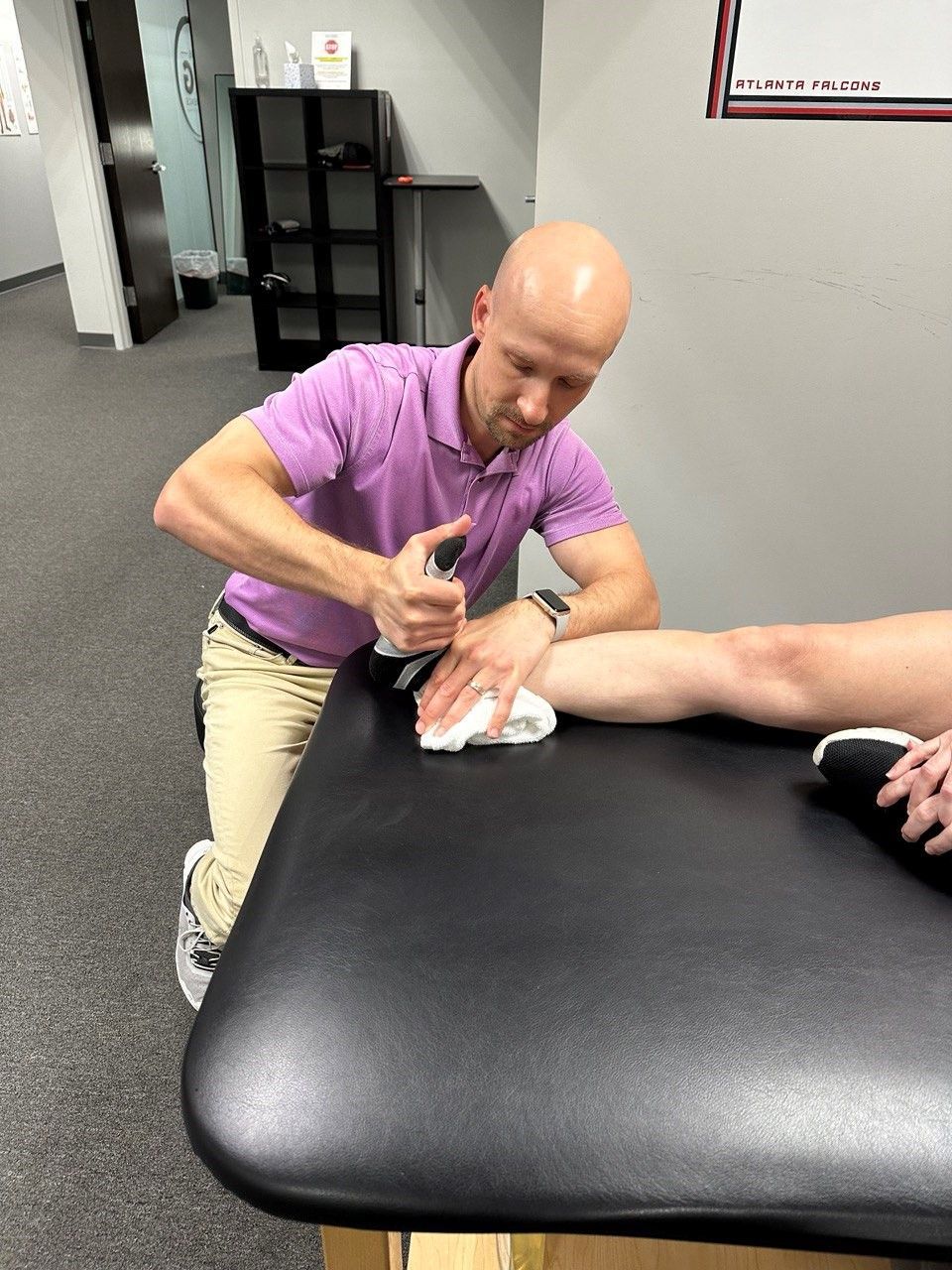 A man in a purple shirt is working on a person 's ankle