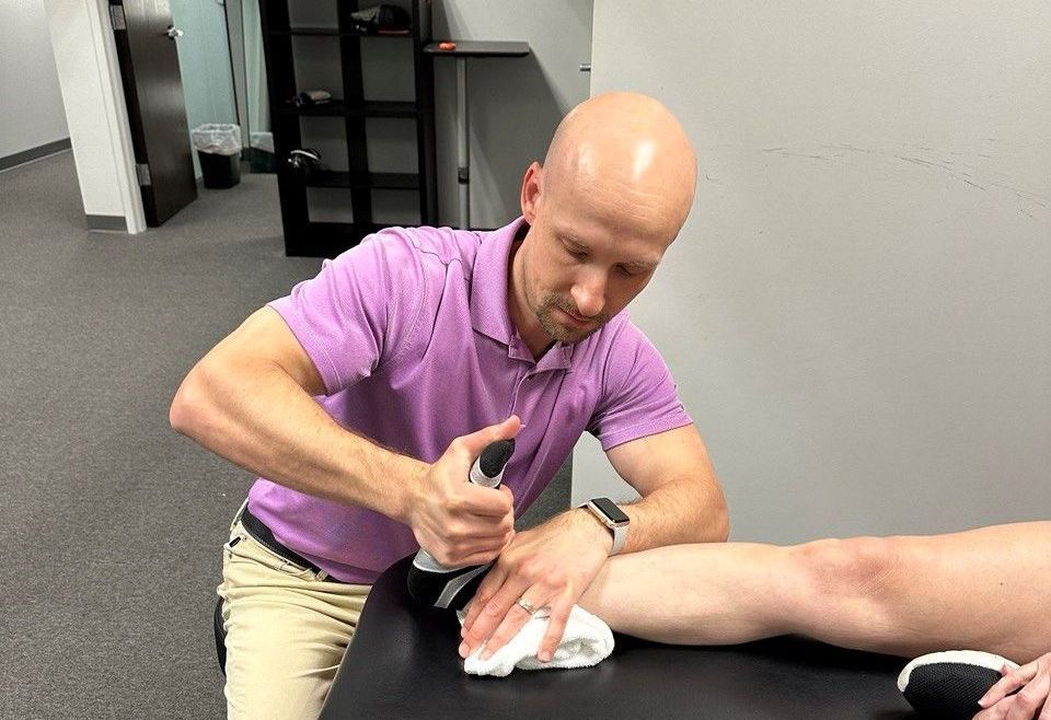 A man in a purple shirt is giving a person a massage on their leg.